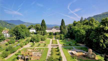 Luftaufnahme der Gartenanlage im Parc de Wesserling mit Schloss und Vogesen im Hintergrund, Elsass