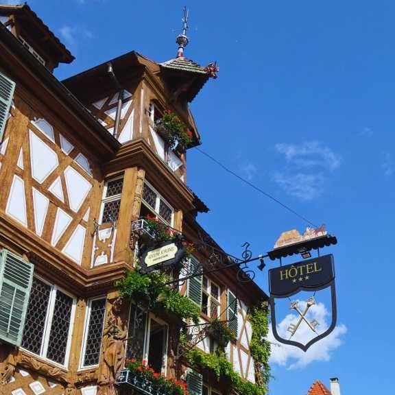 Fachwerkfassade des Hôtel des Deux Clefs in Turckheim mit historischem Hotelschild und Blumenschmuck