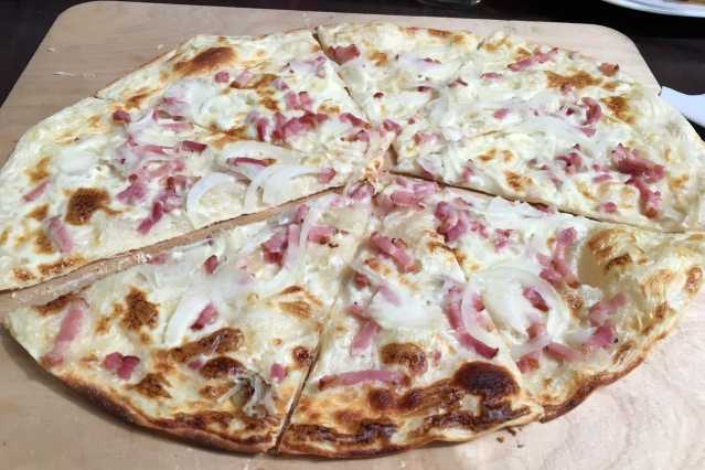 Traditioneller Elsässer Flammkuchen frisch aus dem Ofen – belegt mit Speck, Zwiebeln und Crème fraîche