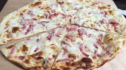 Traditioneller Elsässer Flammkuchen frisch aus dem Ofen – belegt mit Speck, Zwiebeln und Crème fraîche