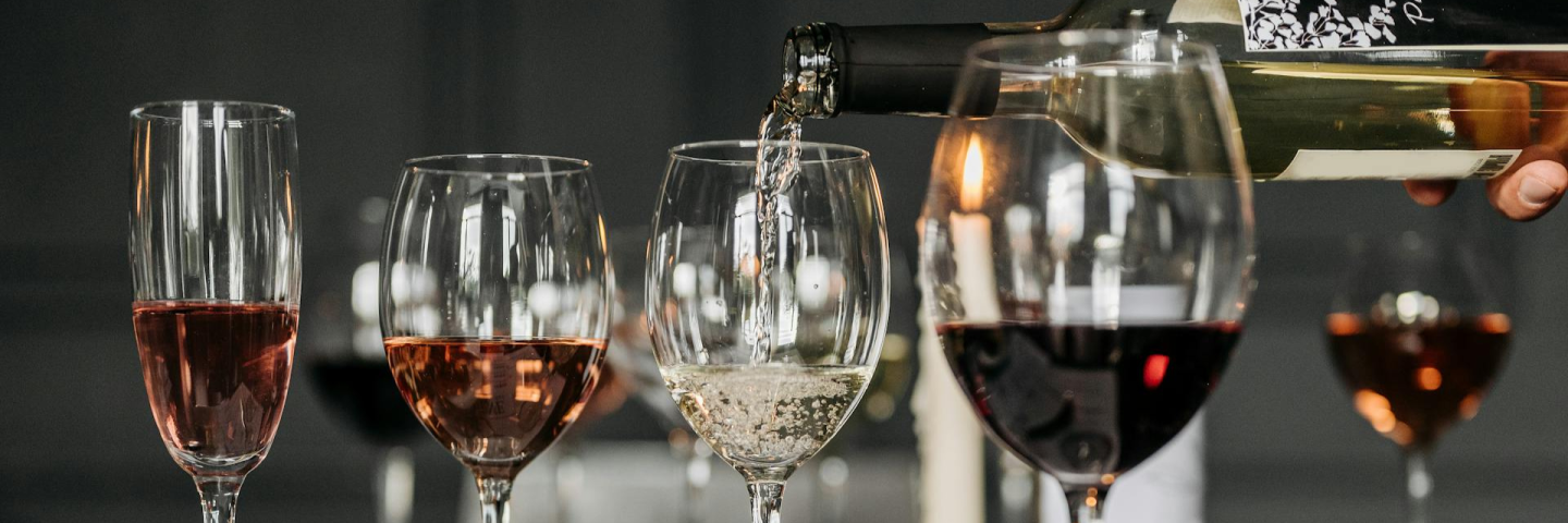 Weingläser mit Rot-, Rosé- und Weißwein – ein Glas wird eingeschenkt, stimmungsvolle Atmosphäre mit Kerzenlicht